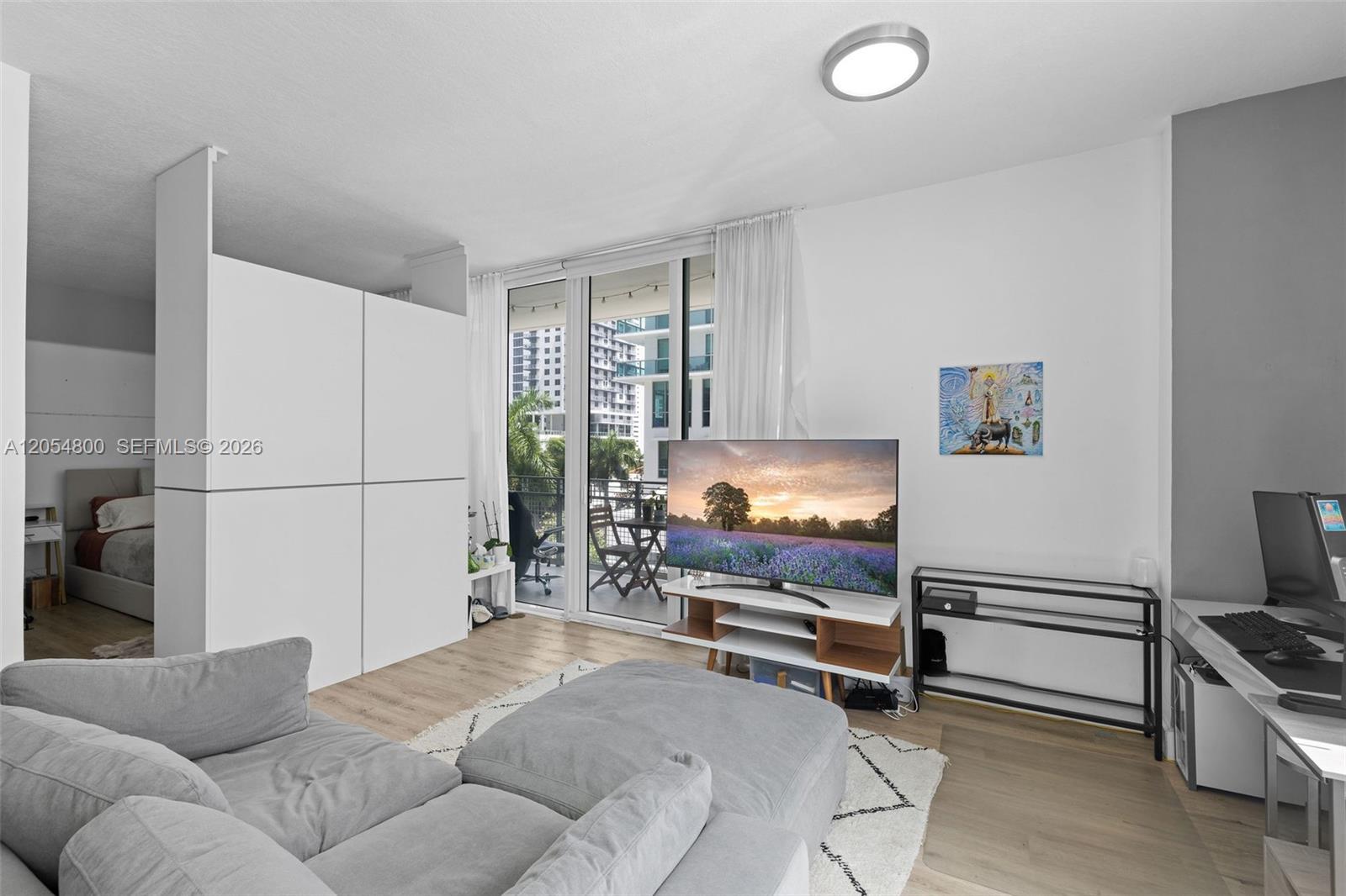 A living room features a grey sectional sofa, a television on a stand, and a balcony — 350 NE 24th St # 401, Miami FL 33137, MIAMI, FL