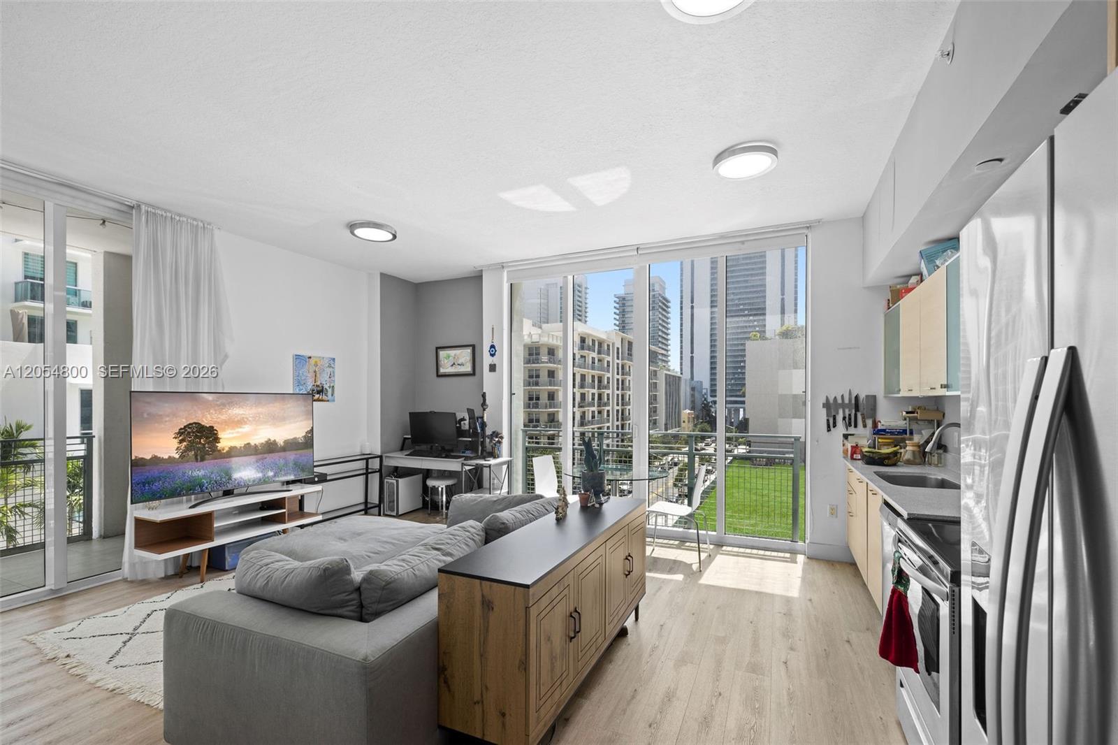 A modern open-concept living area features a kitchen, sofa, desk, and floor-to-ceiling windows with balcony access — 350 NE 24th St # 401, Miami FL 33137, MIAMI, FL