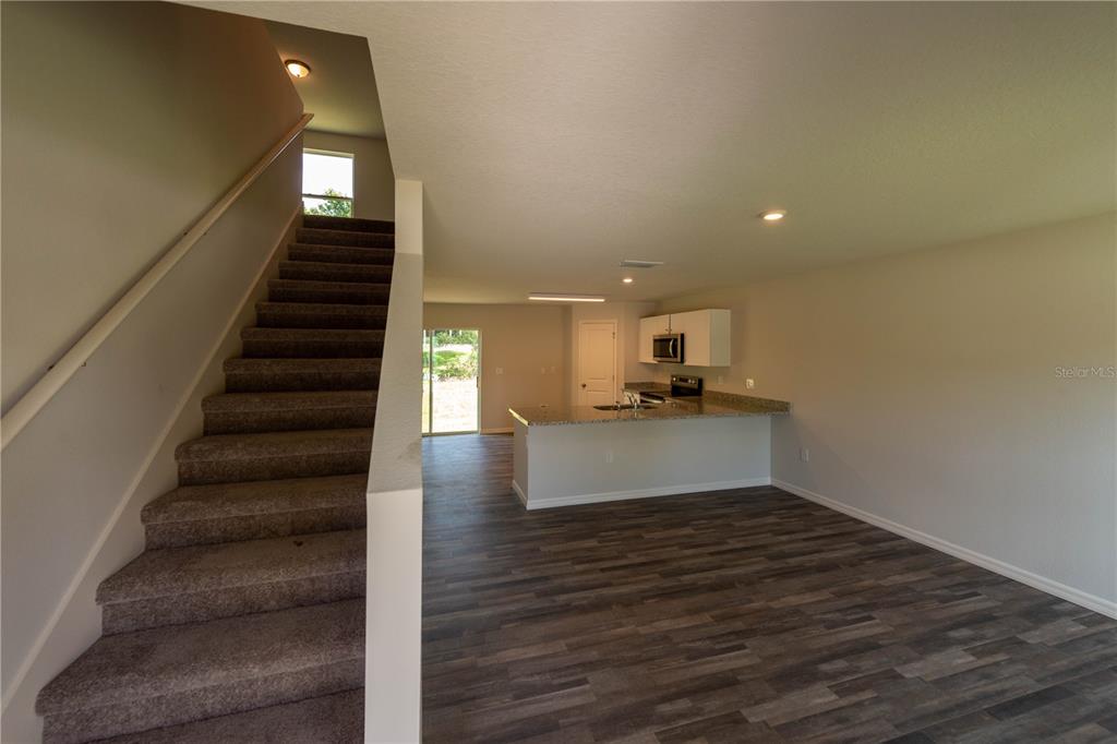 A carpeted staircase leads to an upper level beside an open kitchen and living area — 3427 HARTLEY ROAD, SPRING HILL, FL