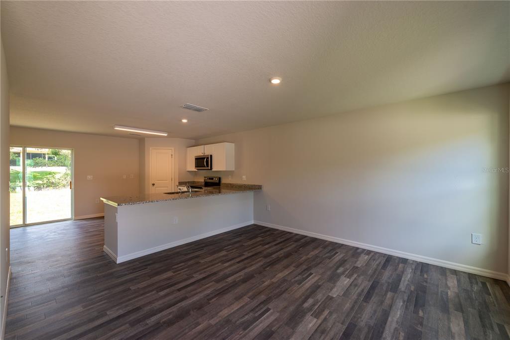 An open-concept kitchen with a breakfast bar overlooks a living area with wood-look flooring — 3427 HARTLEY ROAD, SPRING HILL, FL