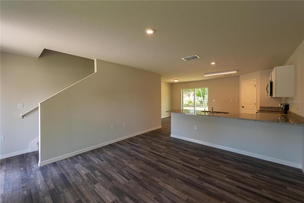 An open-concept living area features wood-look flooring, a staircase, and a kitchen with granite countertops — 3427 HARTLEY ROAD, SPRING HILL, FL