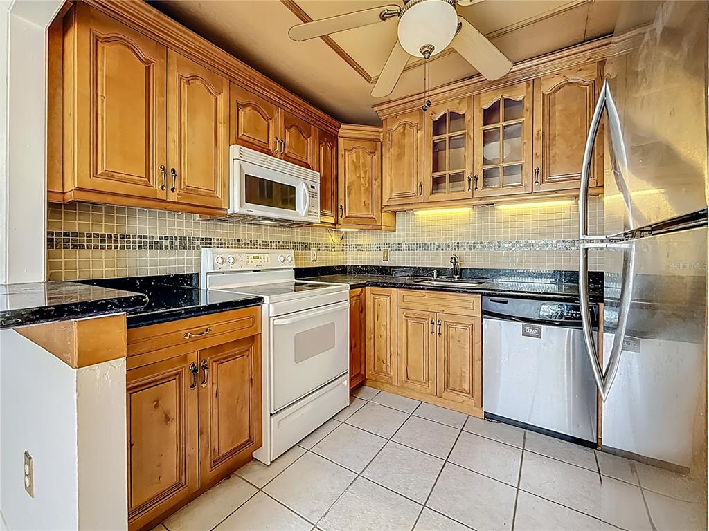 A kitchen features wood cabinets, black countertops, a white stove, and a stainless steel dishwasher — 379 S MCMULLEN BOOTH ROAD UNIT 76, CLEARWATER, FL