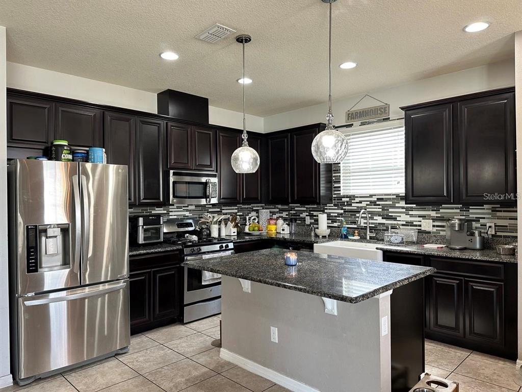 A kitchen features dark wood cabinets, granite countertops, stainless steel appliances, and a central island — 12254 SANDY APPLE ROAD, ORLANDO, FL