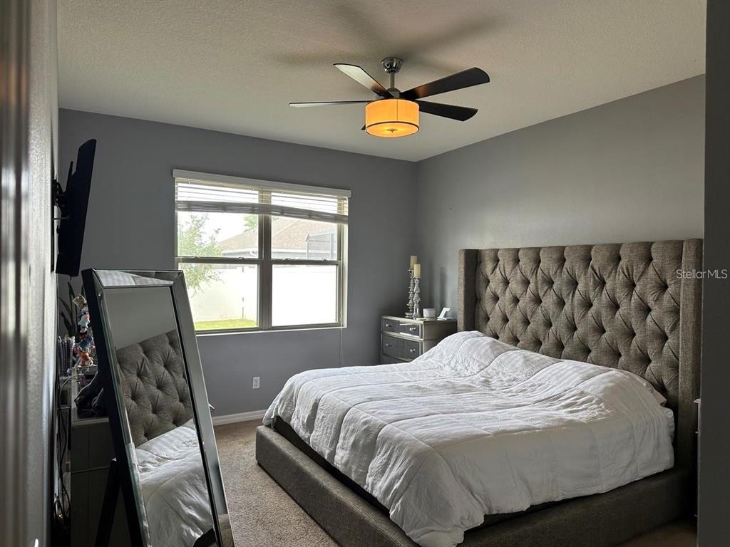 A bedroom features a tufted gray headboard, a large floor mirror, and a ceiling fan — 12254 SANDY APPLE ROAD, ORLANDO, FL