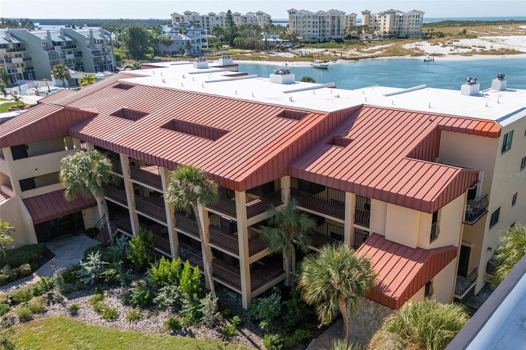 An aerial view shows a multi-story building with a red metal roof near water — 1060 PINELLAS BAYWAY S UNIT 106, TIERRA VERDE, FL