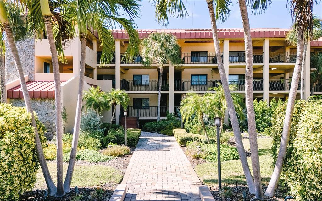 An exterior view of a multi-story apartment building with balconies, palm trees, and a walkway — 1060 PINELLAS BAYWAY S UNIT 106, TIERRA VERDE, FL