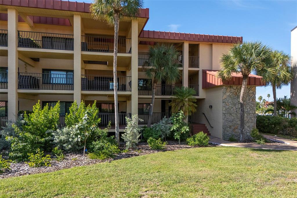 A multi-story apartment building with balconies, palm trees, and a stone-accented entrance — 1060 PINELLAS BAYWAY S UNIT 106, TIERRA VERDE, FL