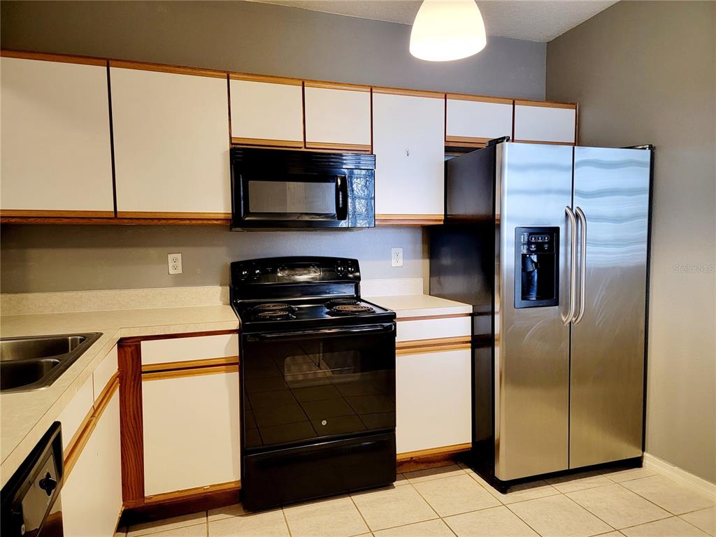 A kitchen features white cabinets with wood trim, black appliances, and light-colored tile flooring — 6410 CYPRESSDALE DRIVE UNIT 201, RIVERVIEW, FL