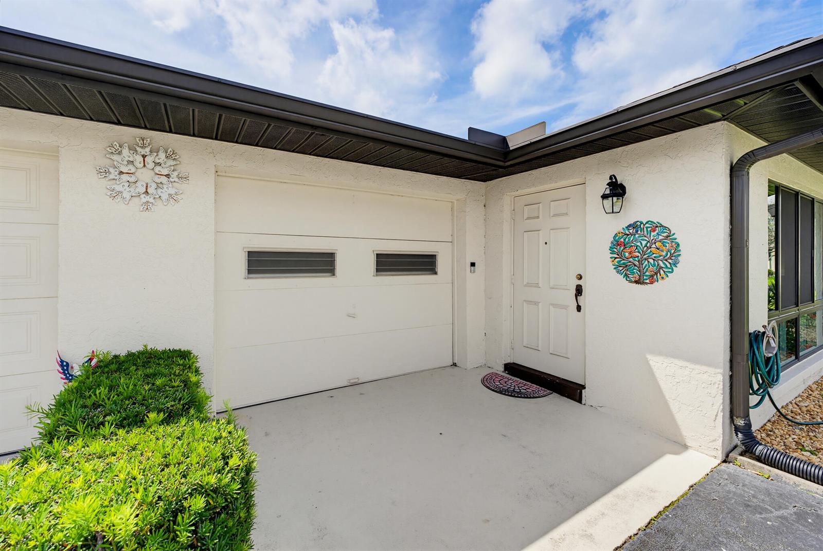 The exterior of a home features a white garage door, a front door, and wall decor — 4854 Equestrian Circle Apt B, Boynton Beach FL 33436, BOYNTON BEACH, FL