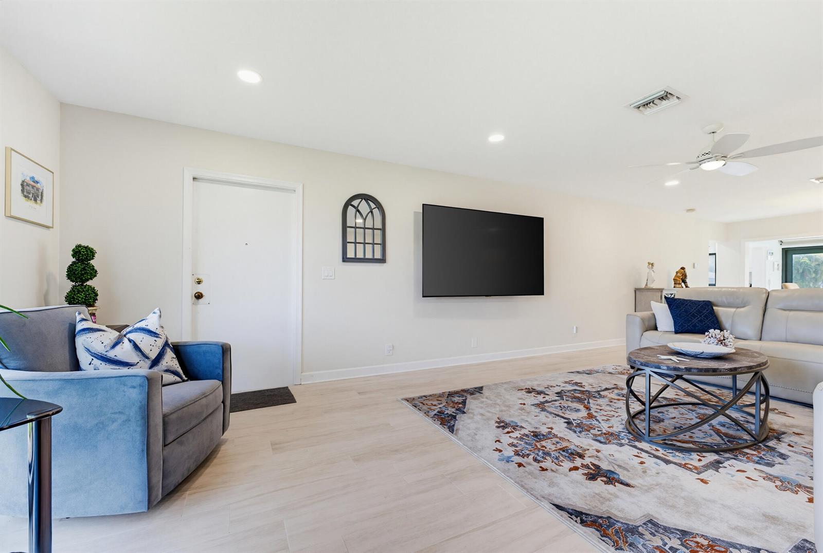 A living room features light wood-look flooring, a wall-mounted television, and a patterned area rug — 4854 Equestrian Circle Apt B, Boynton Beach FL 33436, BOYNTON BEACH, FL