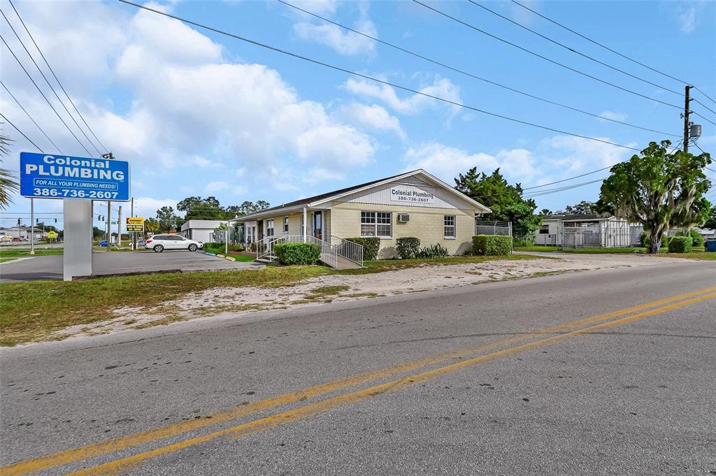 A single-story commercial building with a sign for Colonial Plumbing stands beside a road — 1319 S WOODLAND BOULEVARD, DELAND, FL