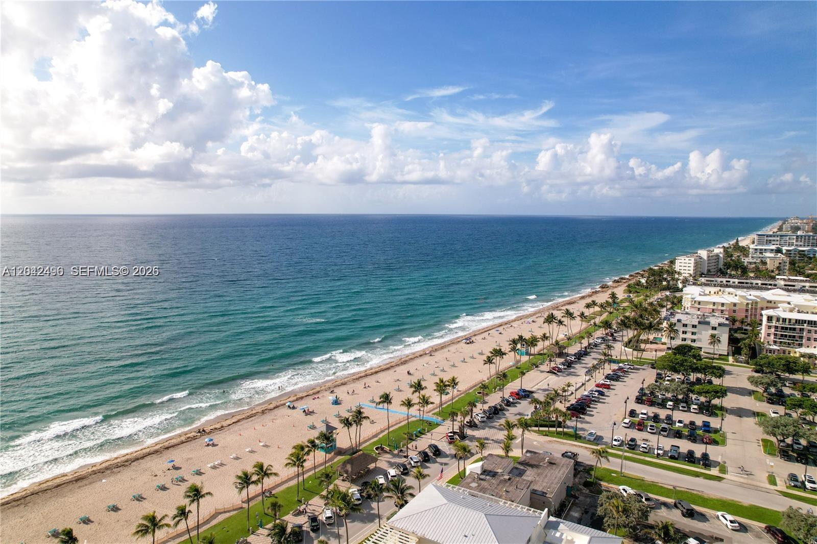 An aerial view shows a sandy beach, ocean, palm trees, and a parking lot — 9 NE 20th Ave # 201, Deerfield Beach FL 33441, DEERFIELD BEACH, FL