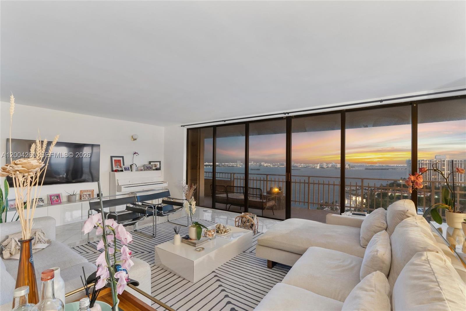 A living room features a white sofa, a striped rug, and floor-to-ceiling windows overlooking water — 11113 Biscayne Blvd # 2051, Miami FL 33181, MIAMI, FL