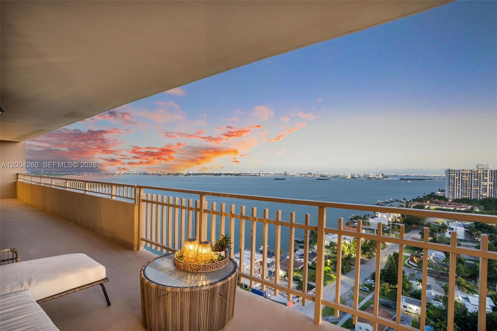 A balcony with a glass-topped table overlooks a bay and a distant city skyline — 11113 Biscayne Blvd # 2051, Miami FL 33181, MIAMI, FL