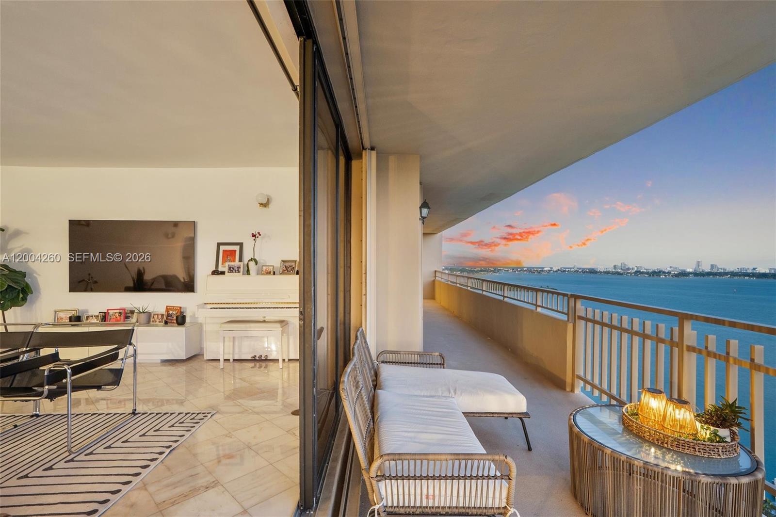 A living room with a white piano opens onto a balcony overlooking the water — 11113 Biscayne Blvd # 2051, Miami FL 33181, MIAMI, FL