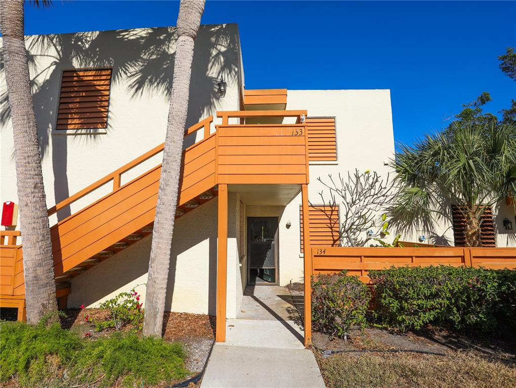 An exterior view of a two-story building with orange wooden stairs and a ground-level entrance — 133 WILD PALM DRIVE UNIT 133, BRADENTON, FL