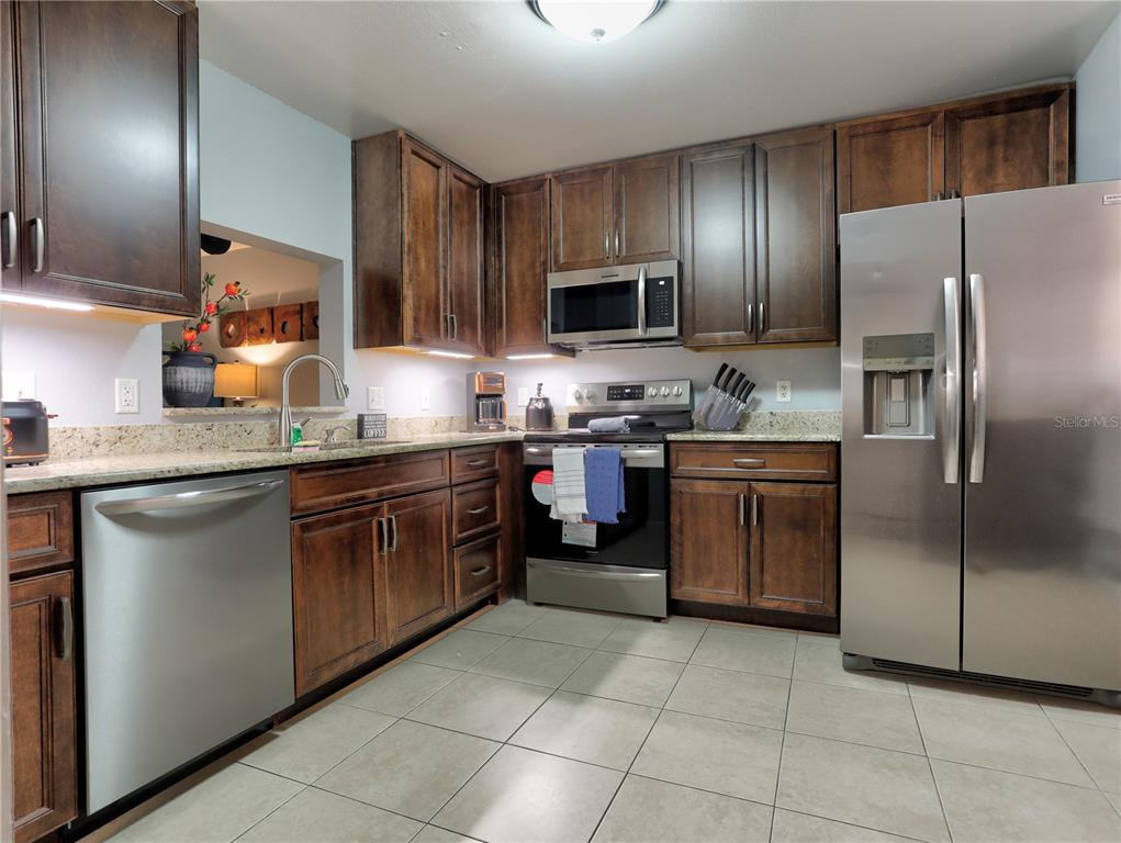 A kitchen features dark wood cabinets, stainless steel appliances, and light-colored tile flooring — 133 WILD PALM DRIVE UNIT 133, BRADENTON, FL