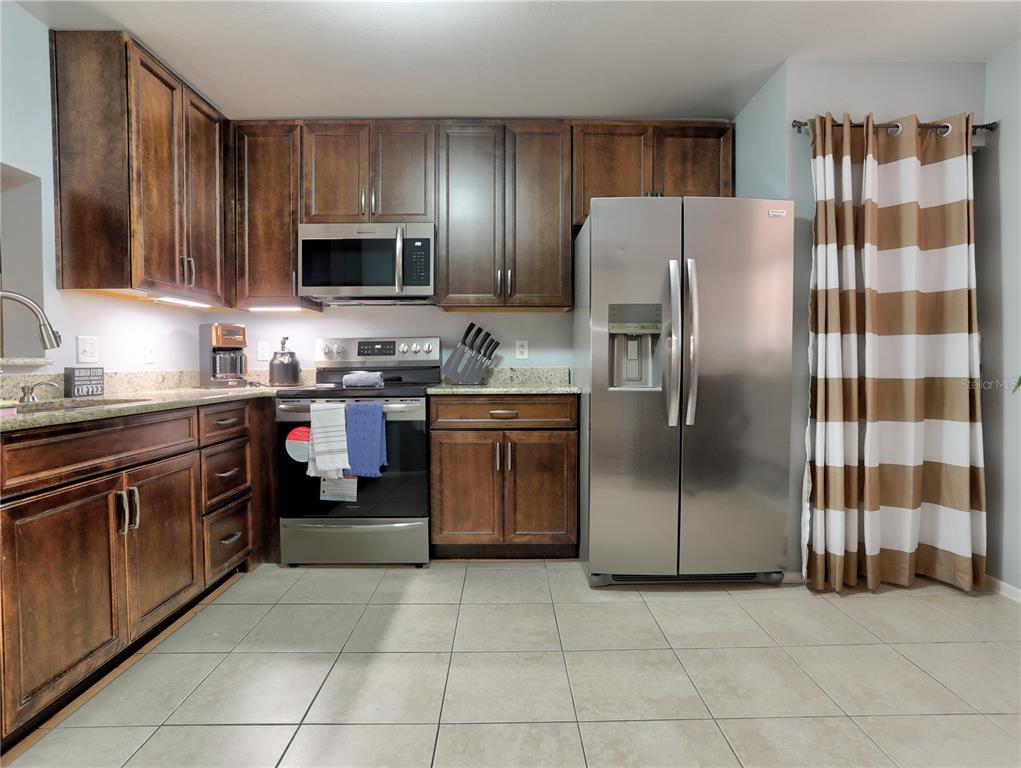 A kitchen features dark wood cabinets, stainless steel appliances, granite countertops, and light tile flooring — 133 WILD PALM DRIVE UNIT 133, BRADENTON, FL