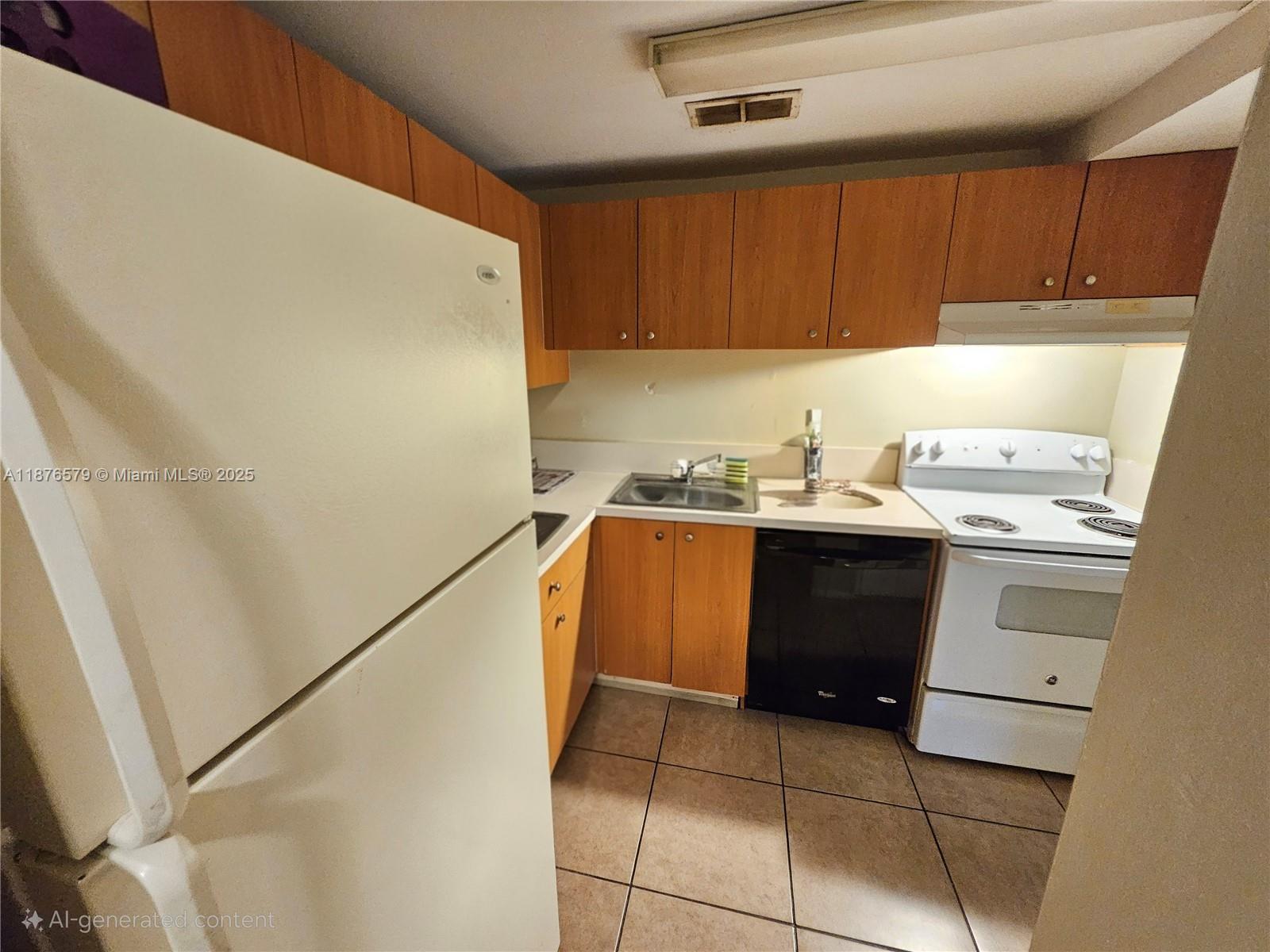 A small kitchen features wood cabinets, white appliances, a black dishwasher, and tiled flooring — 411 Executive Center Dr # 209, West Palm Beach FL 33401, WEST PALM BEACH, FL