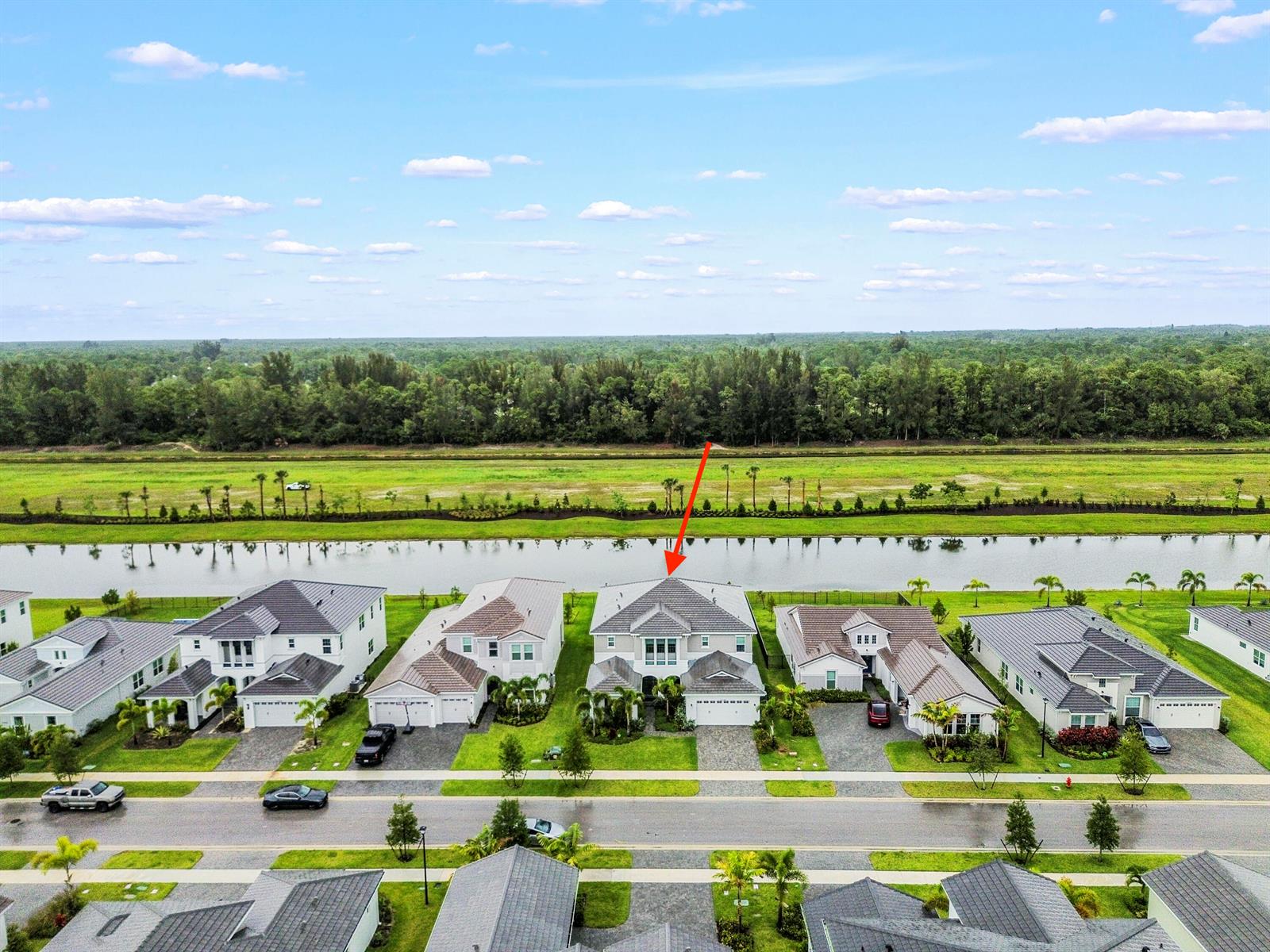 An aerial view shows a suburban neighborhood with houses facing a canal and forest — 15030 Wildwood Circle, Westlake FL 33470, WESTLAKE, FL