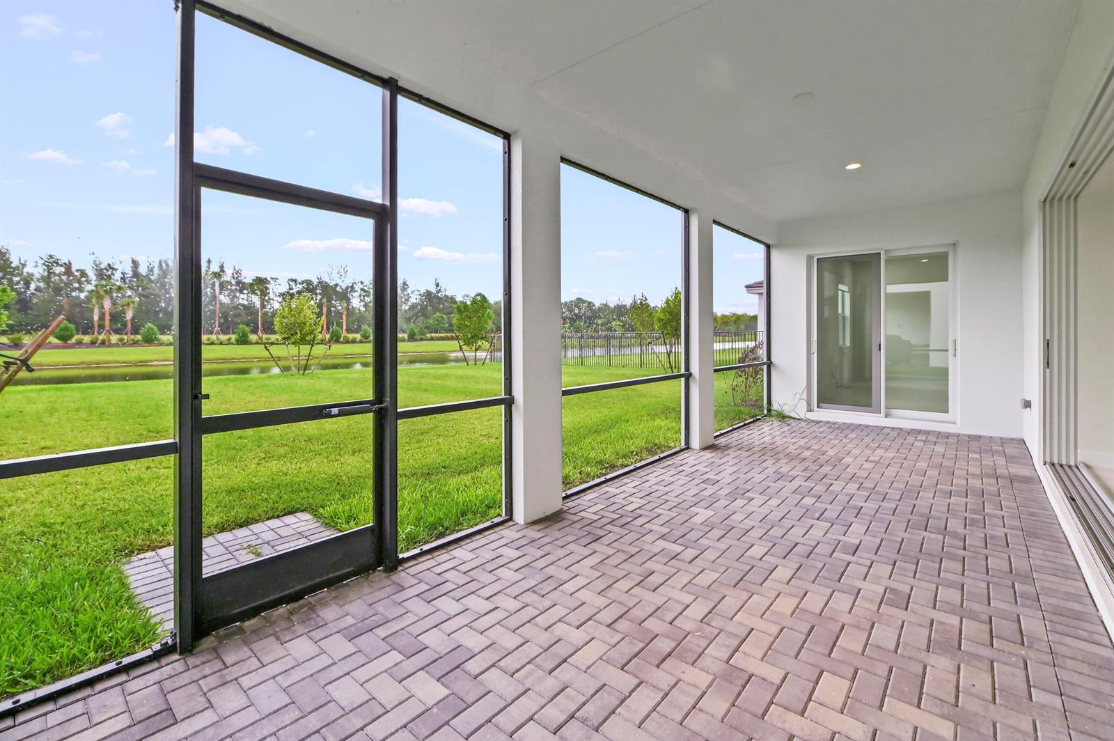 A screened-in patio features gray brick pavers and a view of a grassy backyard — 15030 Wildwood Circle, Westlake FL 33470, WESTLAKE, FL