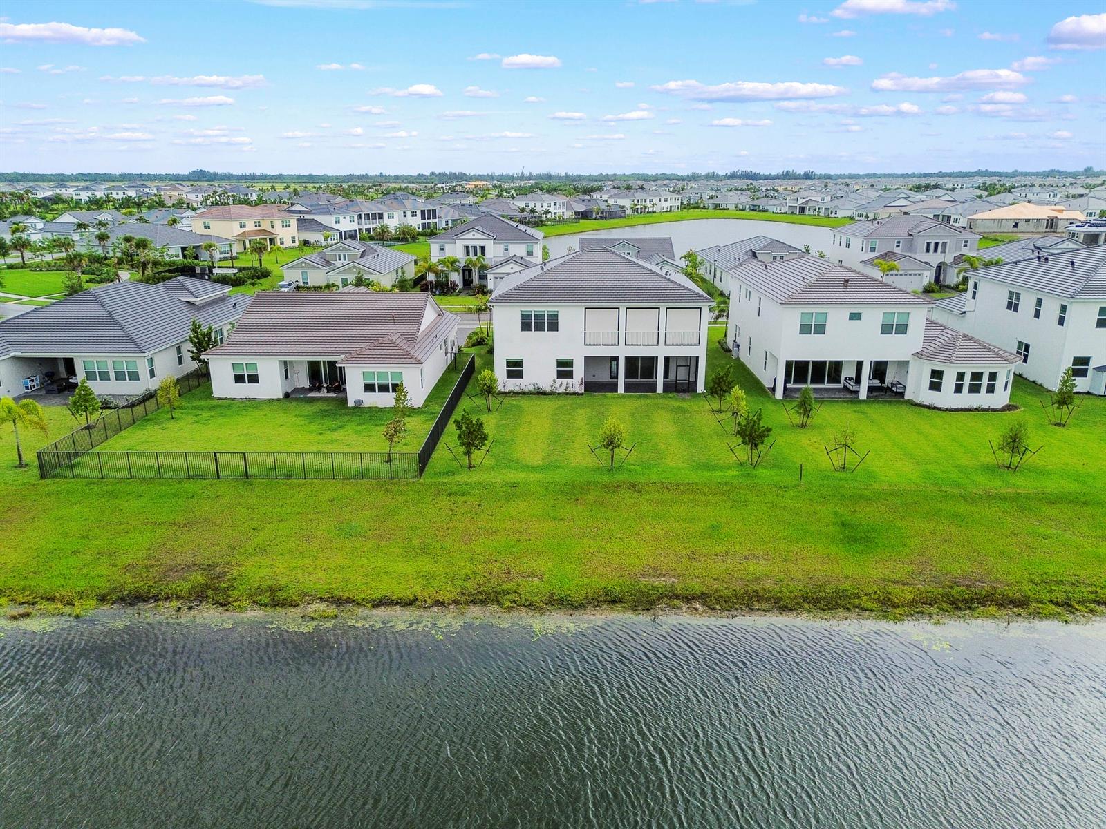 An aerial view shows three white houses with dark roofs overlooking a large pond — 15030 Wildwood Circle, Westlake FL 33470, WESTLAKE, FL