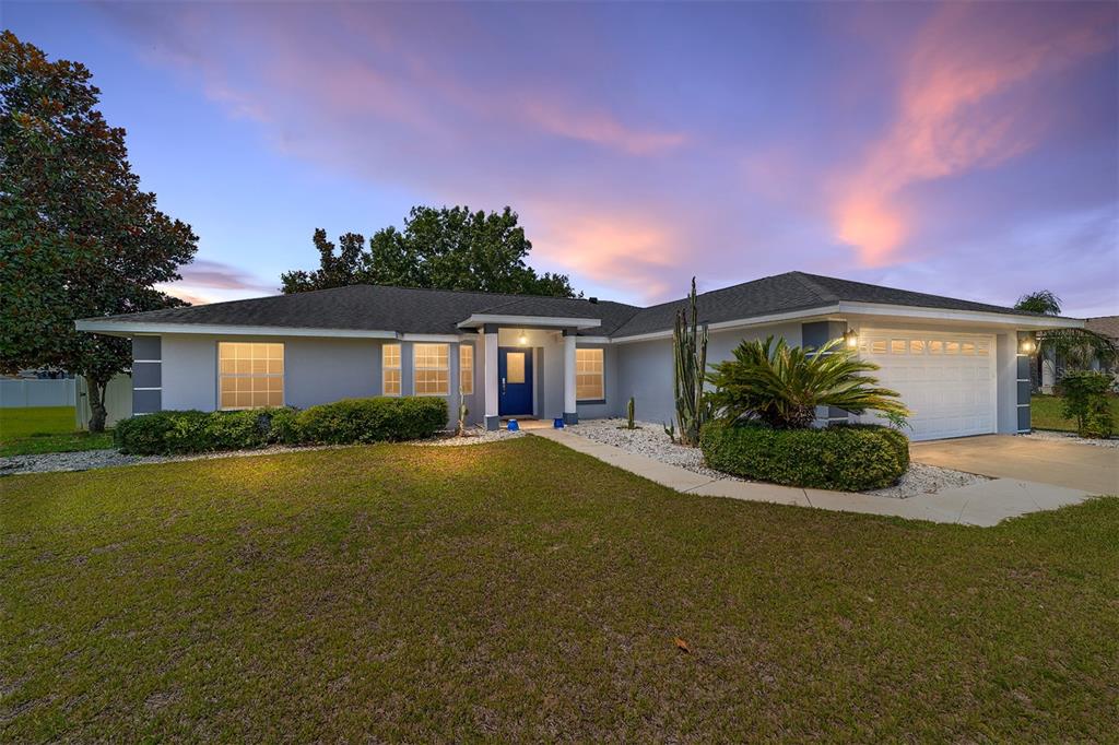 A single-story house with a blue front door, white garage, and a landscaped front yard — 6880 SE 103RD PLACE, BELLEVIEW, FL