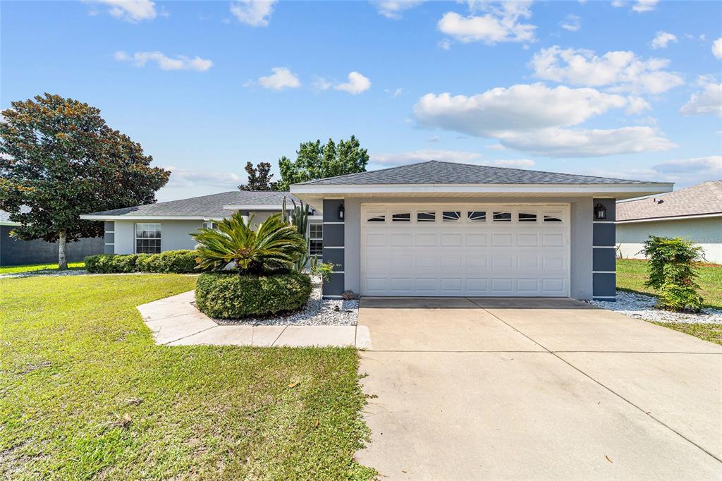 A single-story house with a white garage door, gray trim, and a landscaped front yard — 6880 SE 103RD PLACE, BELLEVIEW, FL