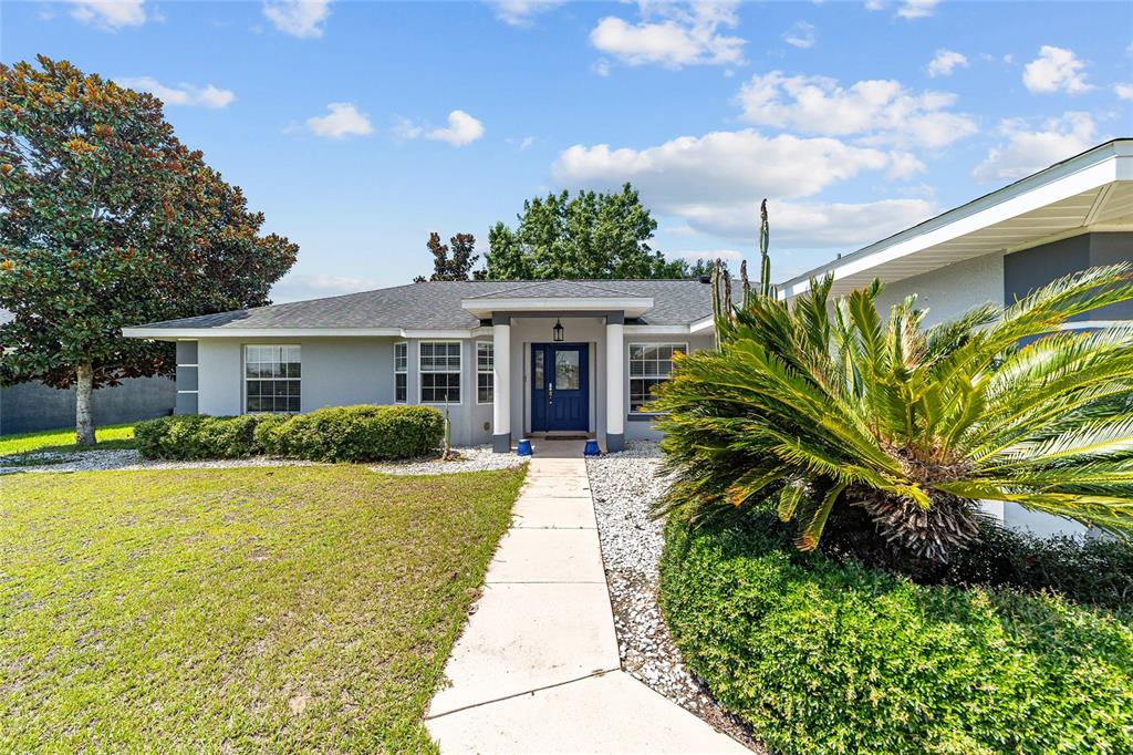 A single-story house with a blue front door, white columns, and a landscaped front yard — 6880 SE 103RD PLACE, BELLEVIEW, FL