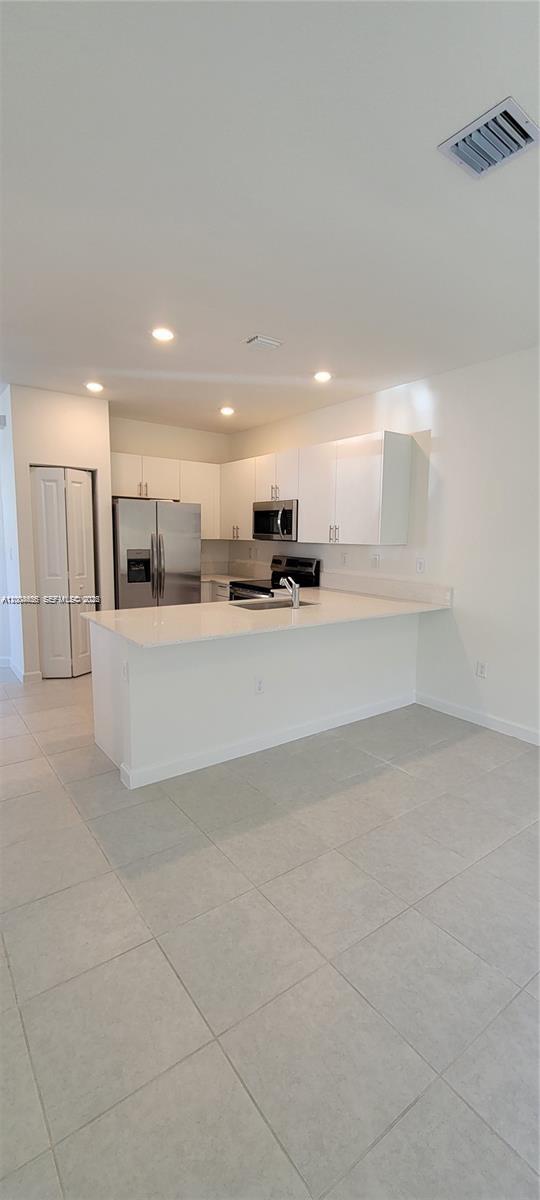 A kitchen features white cabinets, stainless steel appliances, and a white quartz peninsula countertop — 1010 SE 26th Ter, Homestead FL 33035, HOMESTEAD, FL