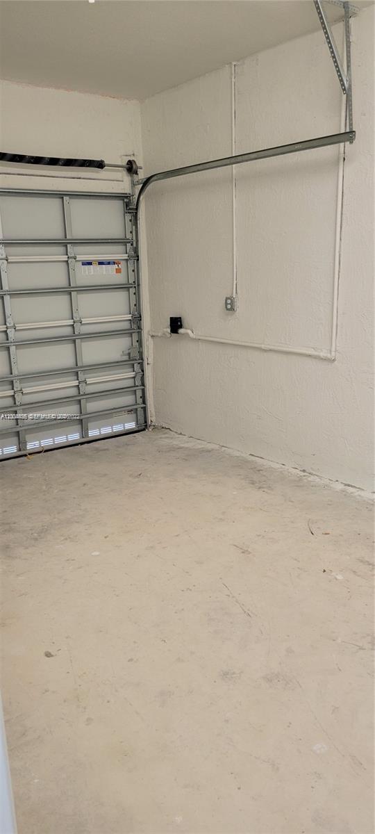 An interior view of a garage with a white roll-up door and exposed wall pipes — 1010 SE 26th Ter, Homestead FL 33035, HOMESTEAD, FL
