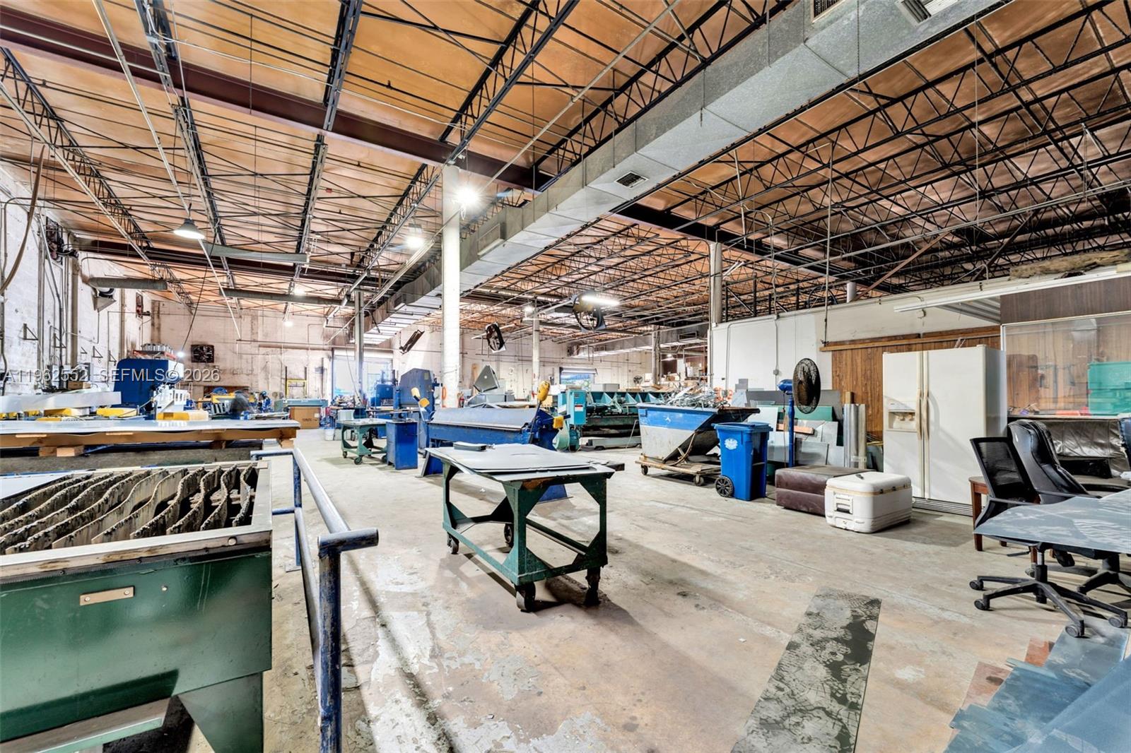 An industrial workshop features exposed ceiling trusses, concrete floors, and various metalworking machinery — 215 W 75th Pl Unit A, Hialeah FL 33014, HIALEAH, FL