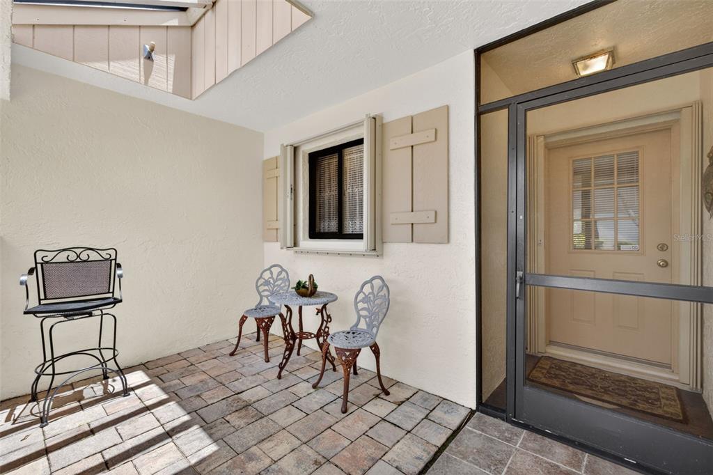A paved patio features a small bistro set, a tall chair, and a screen door — 6072 HUNTINGTON WOODS DRIVE UNIT 17, NAPLES, FL