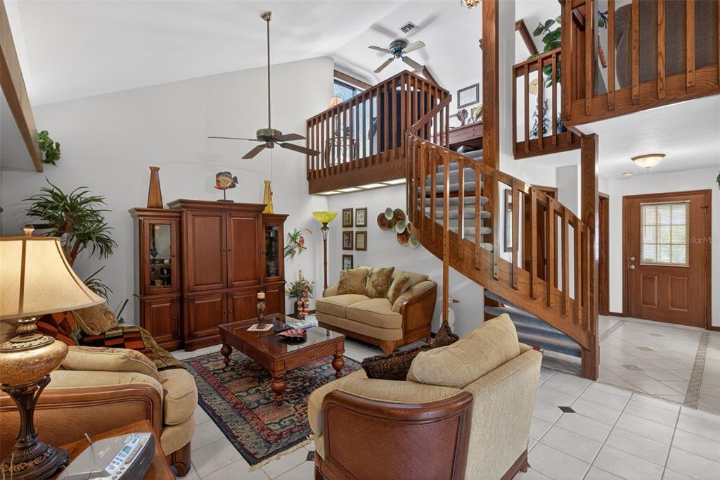 A living room features a wooden spiral staircase, a loft balcony, and tile flooring — 6072 HUNTINGTON WOODS DRIVE UNIT 17, NAPLES, FL