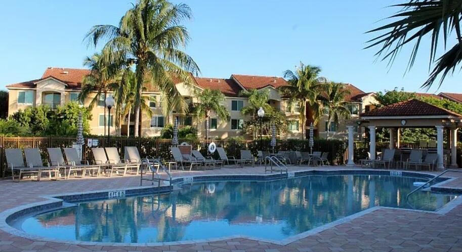A swimming pool sits in front of a multi-story apartment building with palm trees — 1119 Villa Lane # 1119, Boynton Beach FL 33435, BOYNTON BEACH, FL