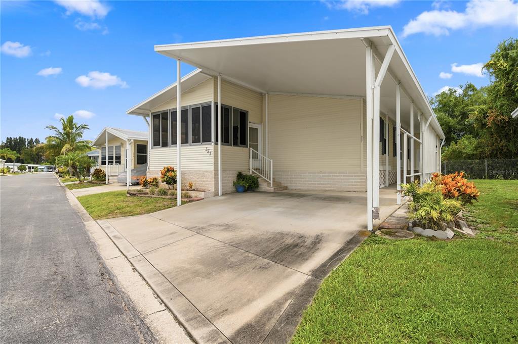 A light-colored mobile home features a screened-in porch, a concrete driveway, and a carport — 9790 66TH STREET N UNIT 357, PINELLAS PARK, FL