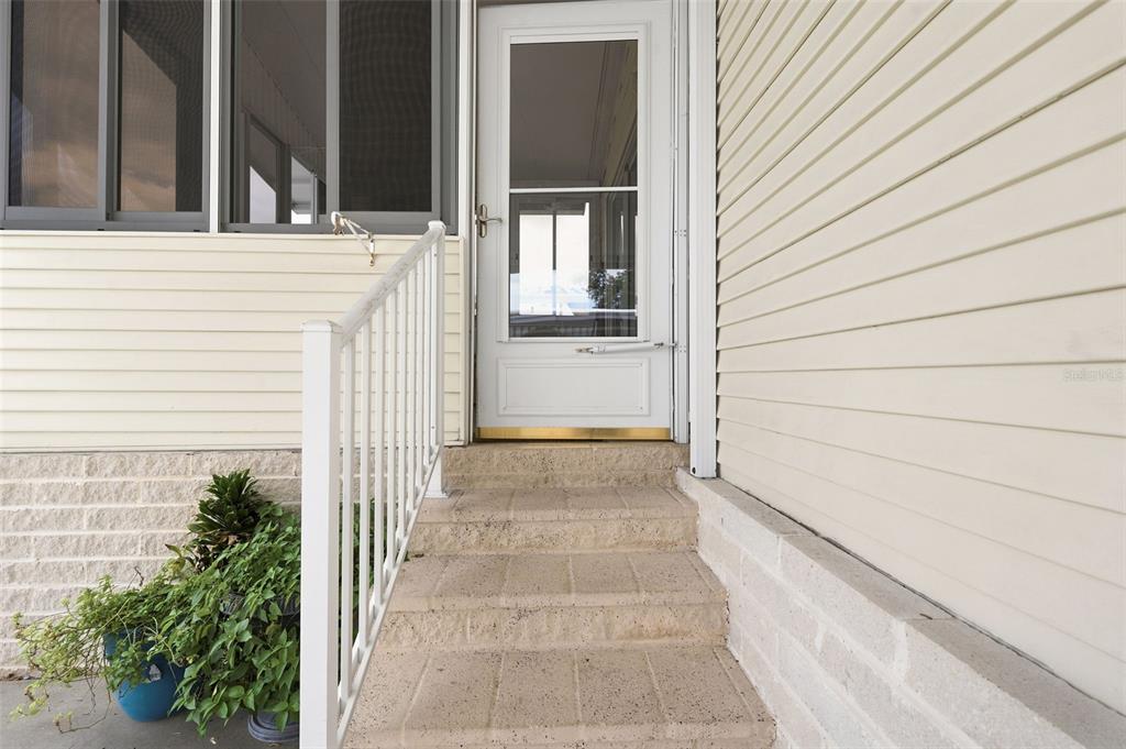 A white storm door leads to concrete steps with a white railing beside beige siding — 9790 66TH STREET N UNIT 357, PINELLAS PARK, FL