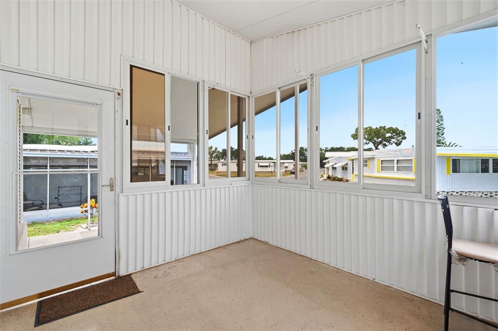 A sunroom with white vertical siding, concrete flooring, and multiple windows looking onto neighboring homes — 9790 66TH STREET N UNIT 357, PINELLAS PARK, FL