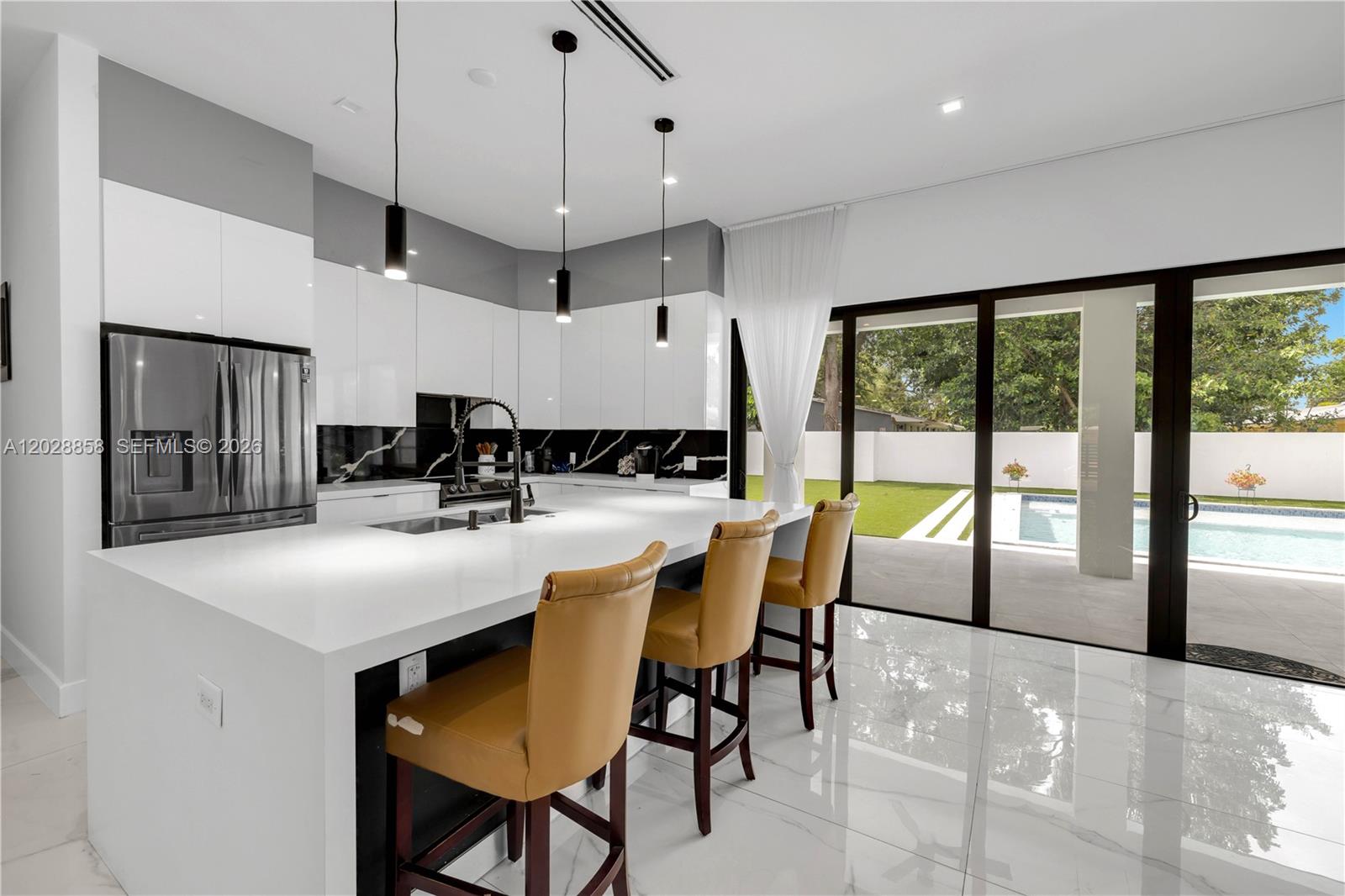 A modern kitchen features white cabinetry, a large island with bar stools, and sliding glass doors — 152 NW 165th St, Miami FL 33169, MIAMI, FL