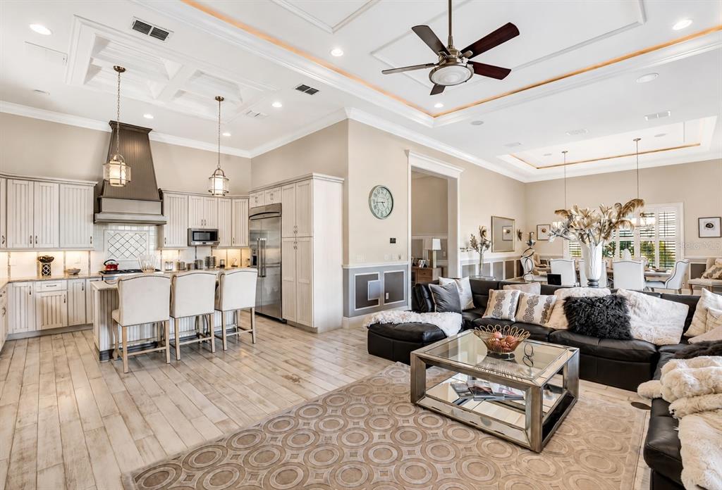 An open-concept kitchen and living room featuring light wood floors, white cabinetry, and coffered ceilings — 7453 GATHERING DRIVE, REUNION, FL