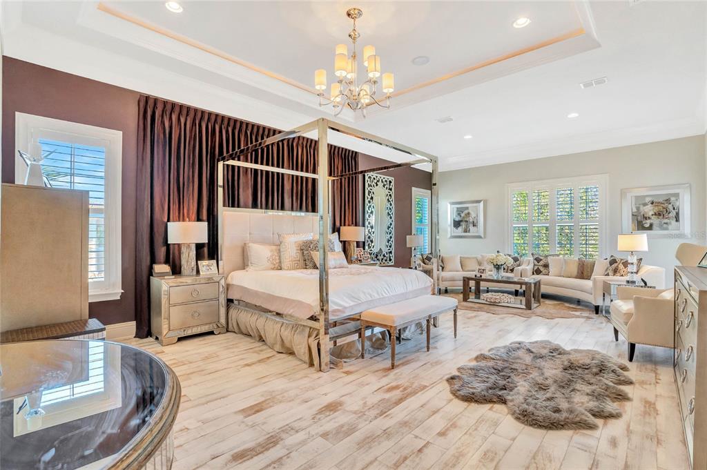 A spacious primary bedroom features a canopy bed, mirrored nightstands, and a seating area — 7453 GATHERING DRIVE, REUNION, FL