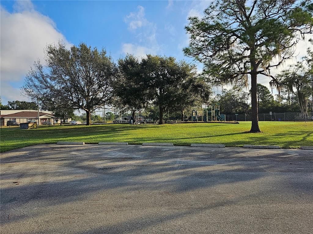 A paved parking lot sits in front of a grassy park with trees and playground equipment — 213 IMAGINATION DRIVE, LAKE PLACID, FL