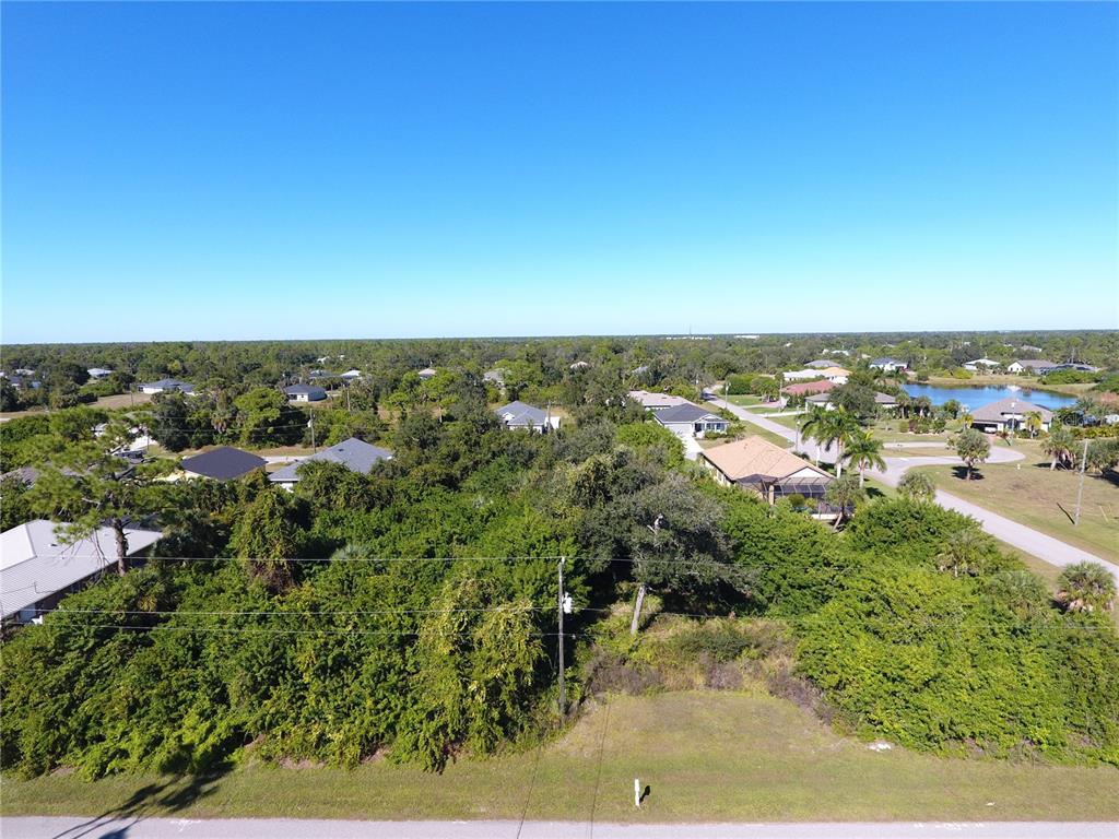 An aerial view shows a vacant, wooded residential lot situated between existing houses and streets — 394 ALBATROSS ROAD, ROTONDA WEST, FL