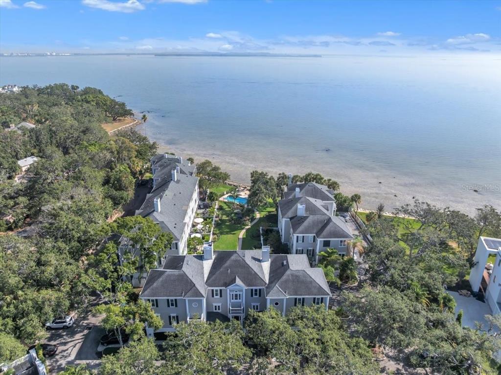 An aerial view shows a multi-story residential complex situated along a waterfront with trees — 6212 BAYSHORE BOULEVARD UNIT K, TAMPA, FL