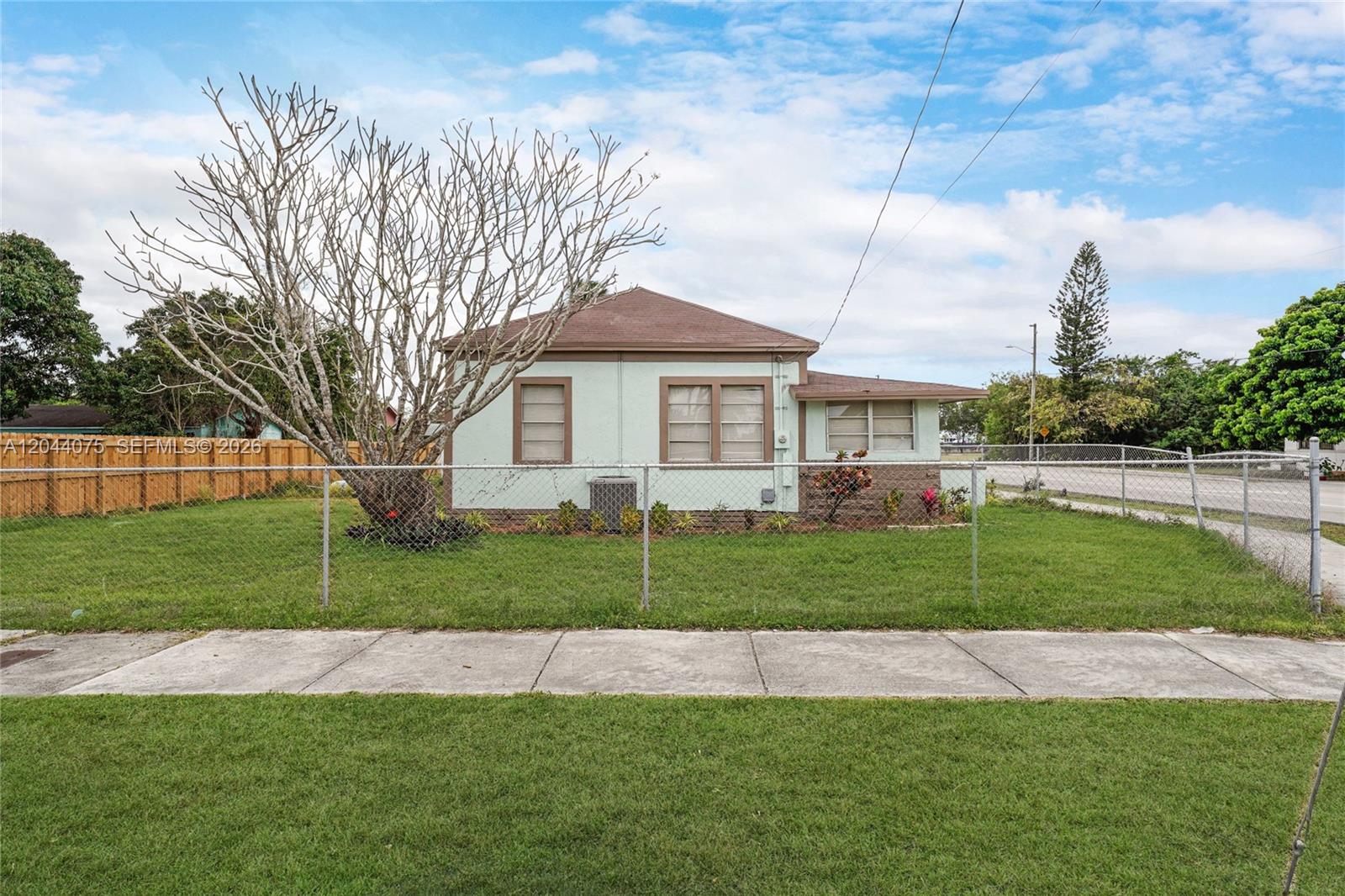 A light green single-story house stands behind a chain-link fence with a large bare tree — 145 NW 6th Ave, Florida City FL 33034, FLORIDA CITY, FL