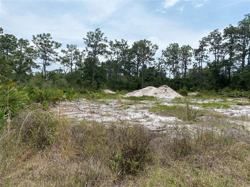 A vacant, sandy lot features patches of low vegetation and a large pile of dirt — 6591 DELAND AVENUE, INDIAN LAKE ESTATES, FL