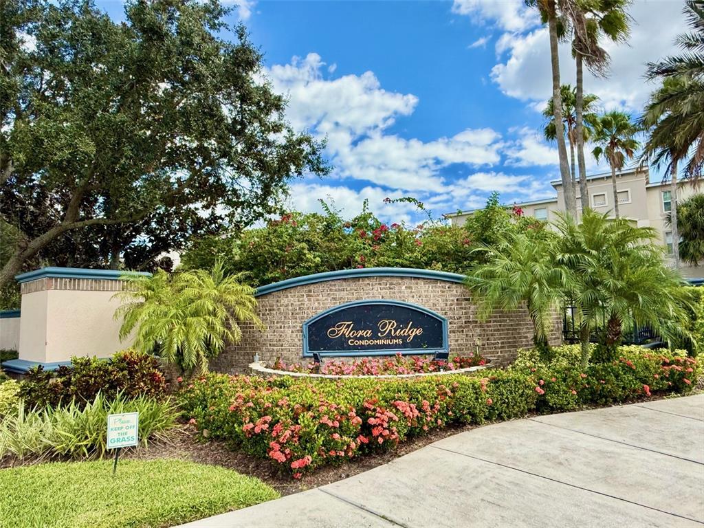 The exterior entrance sign for Flora Ridge Condominiums features a brick wall and landscaping — 3000 LAUREL PARK LANE UNIT 101, KISSIMMEE, FL