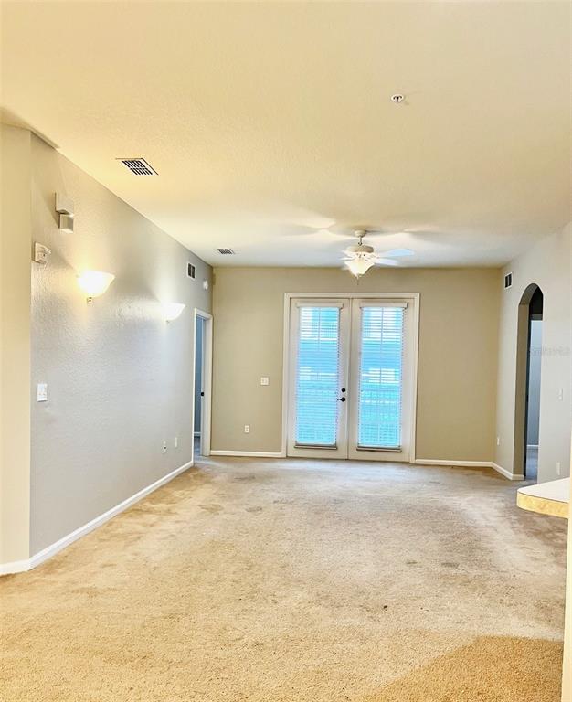 A carpeted living room features a ceiling fan, wall sconces, and glass double doors — 3000 LAUREL PARK LANE UNIT 101, KISSIMMEE, FL