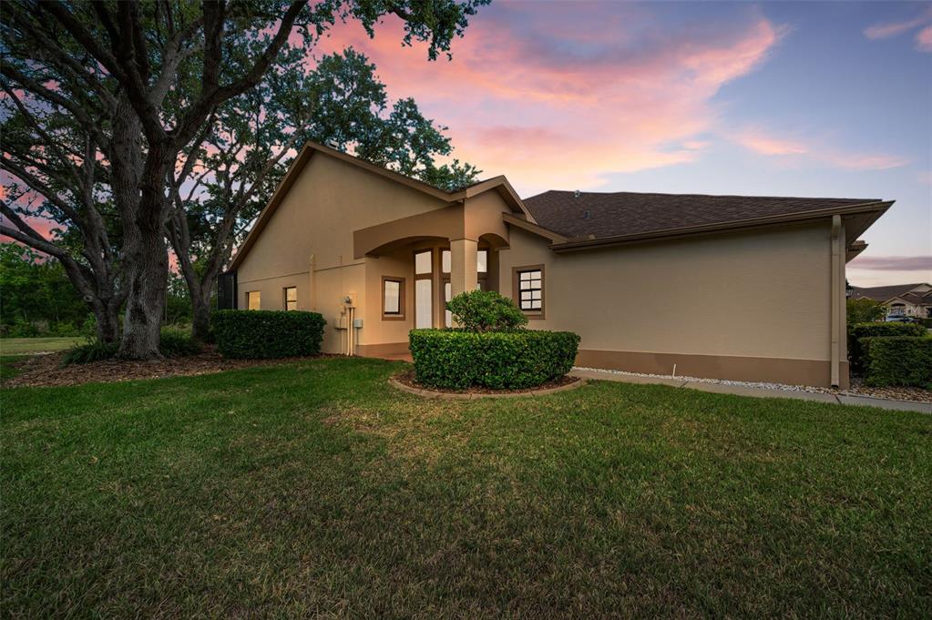 A tan stucco house exterior with a covered entryway and a large tree in front — 9307 PALM HAVEN COURT, NEW PORT RICHEY, FL