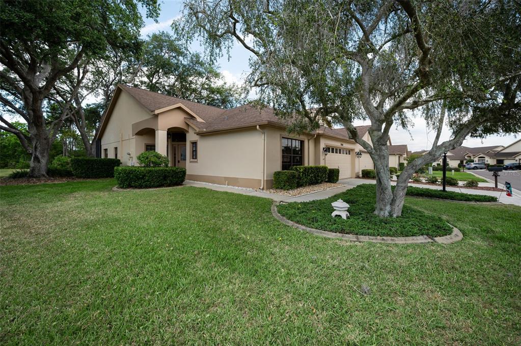 A tan single-story house with a two-car garage and a large tree in the yard — 9307 PALM HAVEN COURT, NEW PORT RICHEY, FL